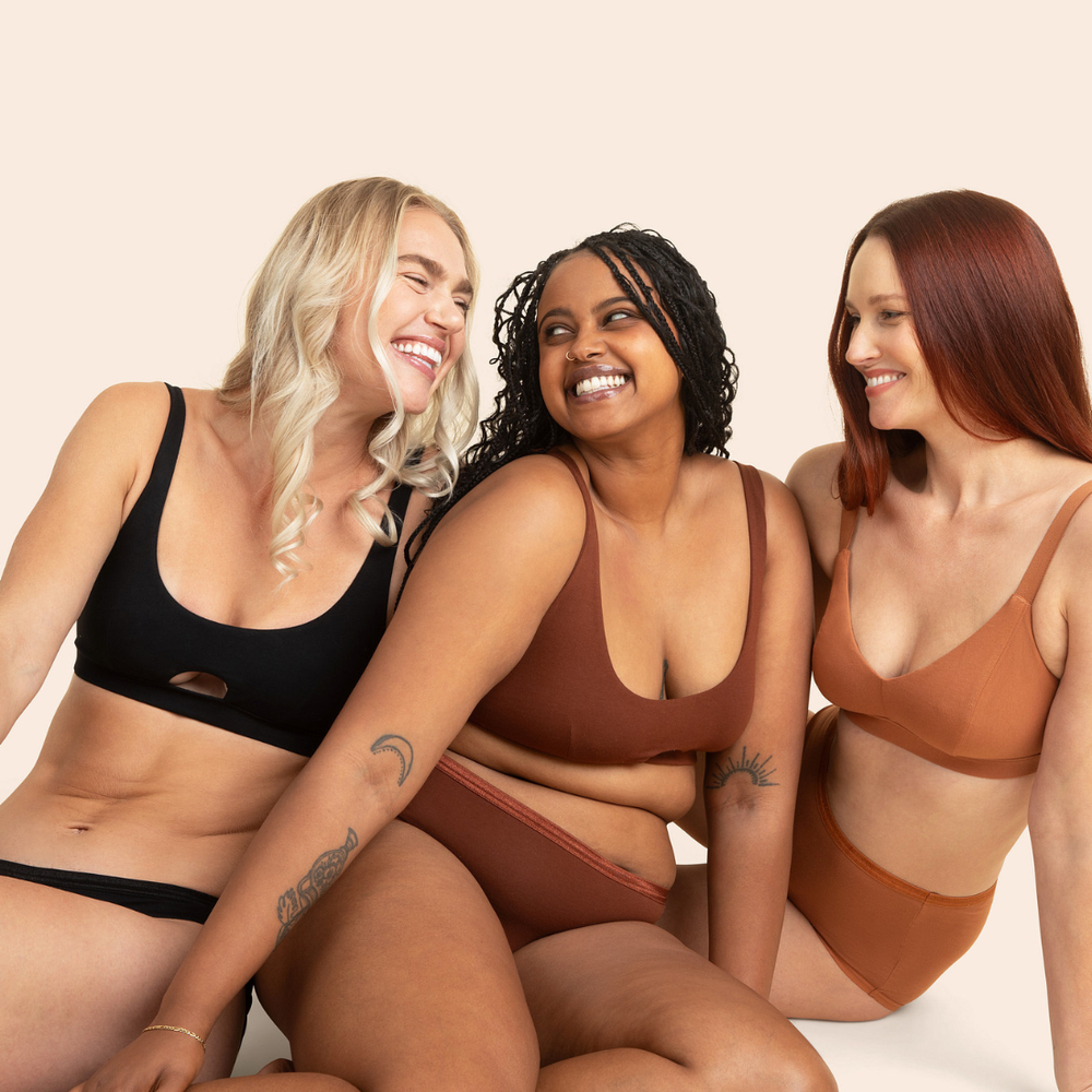 Three women wearing brown and black lingerie sitting together on a beige background